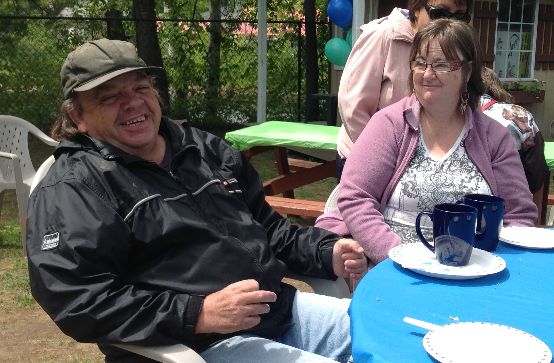 Two participants sitting together outdoors at a table, smiling and enjoying a community gathering