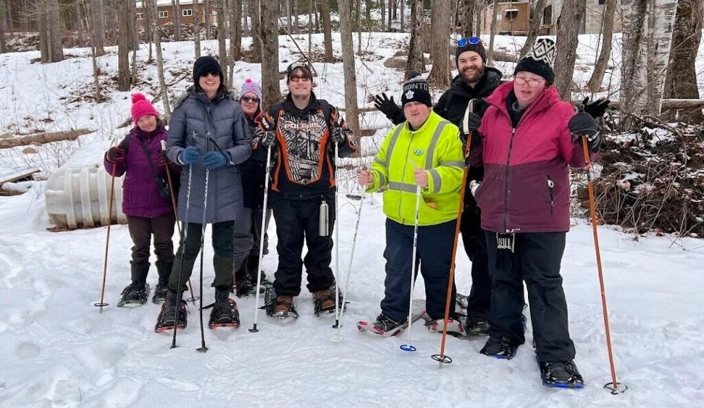 A group of participants snowshoeing together outdoors in winter, standing on a snowy trail surrounded by trees.