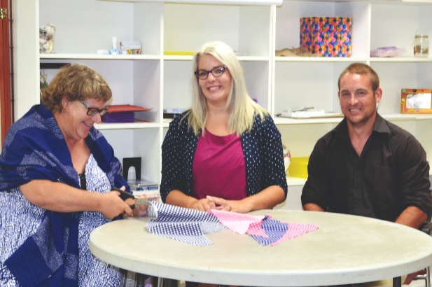 Three people sit at a table with fabric materials during an NHCIA employment and skill-building program.