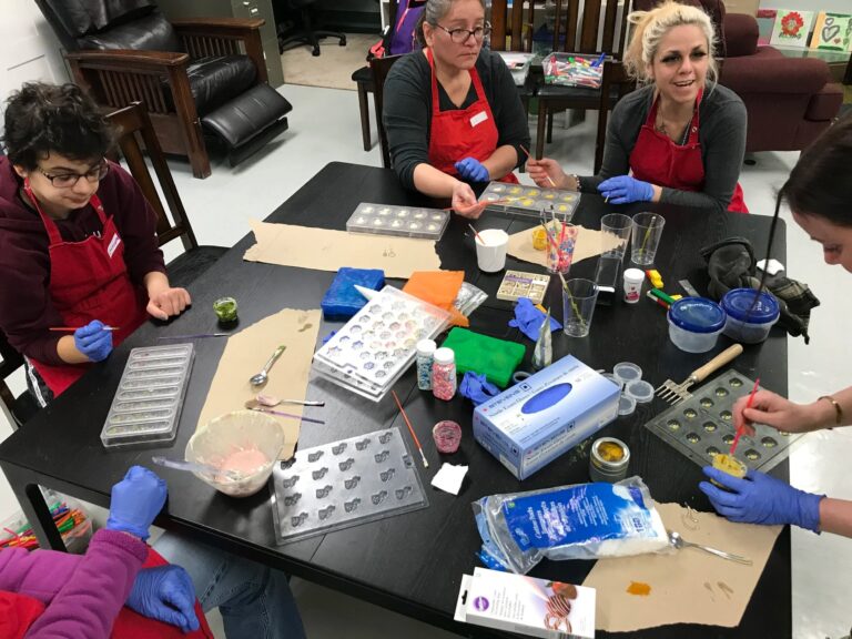 Participants wearing aprons and gloves decorate chocolates during a Kairos Time workshop.